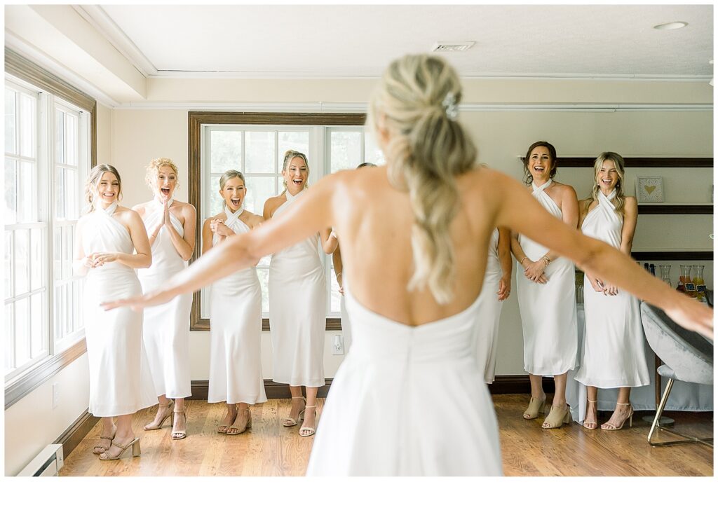 Bridesmaids excitedly look on at bride who reveals her dress for the first time.