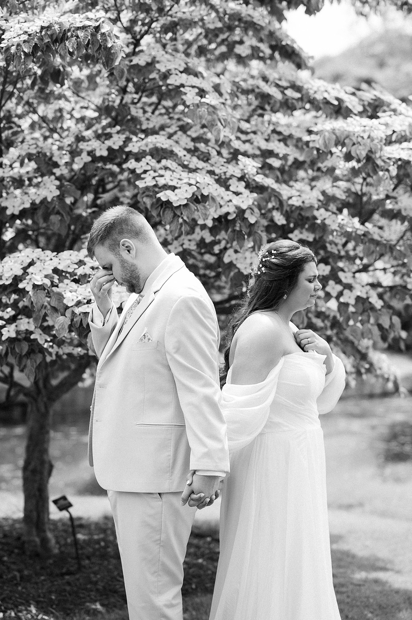 A black and white photo of a bride and groom sharing a private prayer in a garden